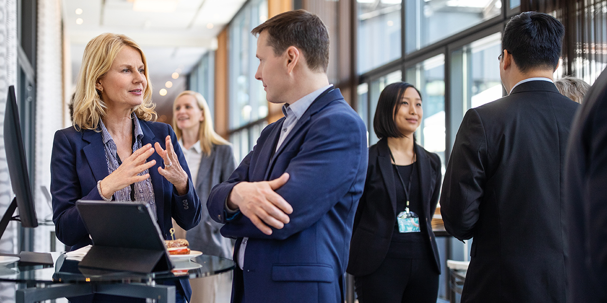 A stock photo of two business people talking to one another on the left, with a group of three business people talking to each other on the right